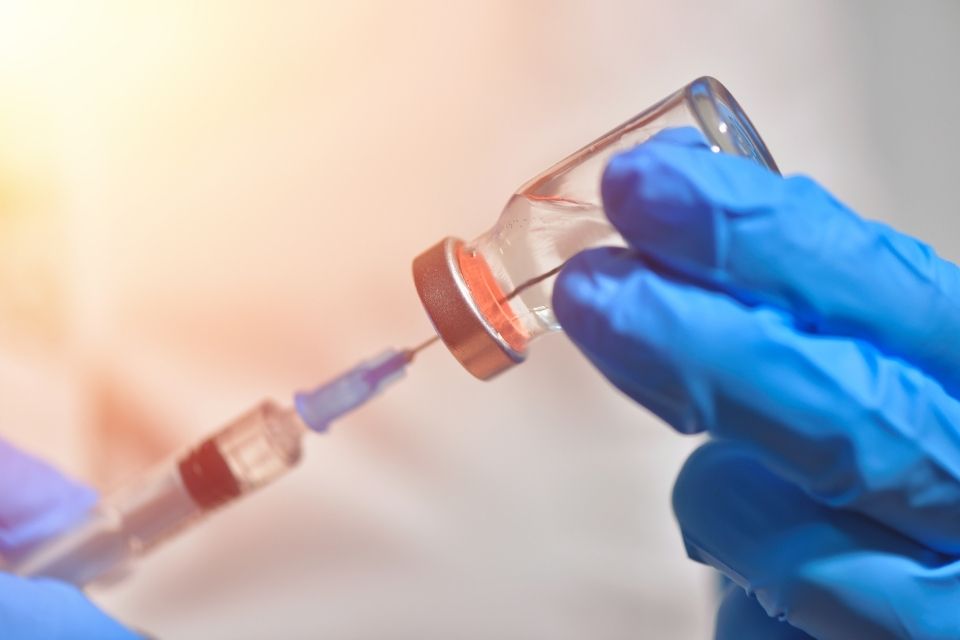 Gloved hands holding a vaccine vial and needle