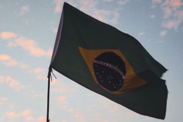 Brazilian flag against light blue sky filled with pink clouds